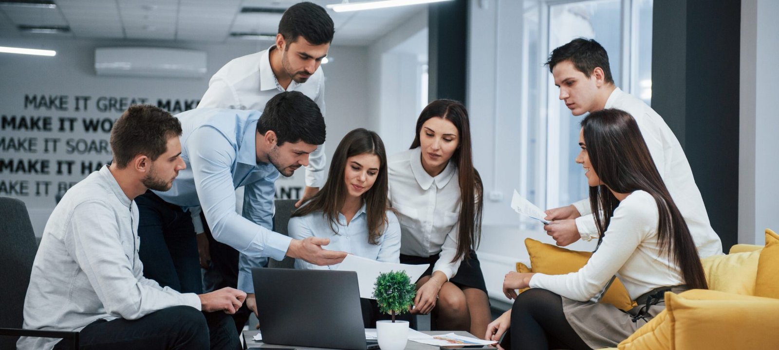 Guy shows document to a girl. Group of young freelancers in the office have conversation and working.